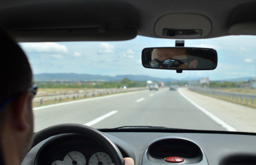 Man driving a car with a dirty front glass after a long drive on a highway with other vehicles blurred in front of him