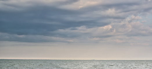 Blue calm sea and sky with  dark clouds. Seascape. Green island on line horizon.