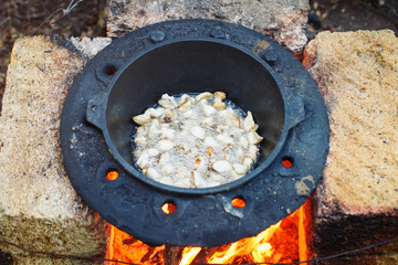 The man cooks national pilaf in a cauldron outdoors.