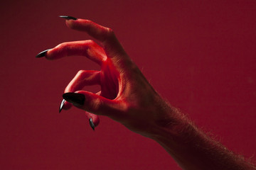 Halloween red devil monster hand with black fingernails against a red background
