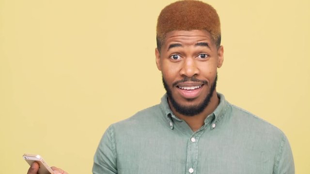 portrait of mulat handsome guy with beard and red hair using mobile phone reading exciting text message pleasant news isolated over yellow background closeup. Concept of emotions
