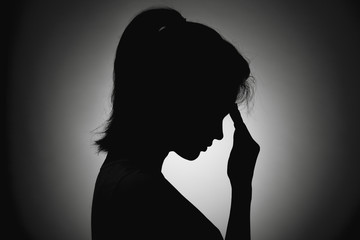 silhouette of the girl face profile of an unrecognizable sad, woman in depression put her hand to...