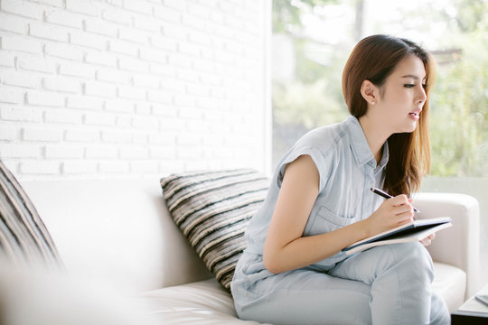 Pretty Asia Woman Writing On Couch At Home In The Living Room