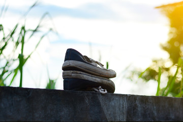 Obraz premium old black-white sport shoes on cement wall near green field with yellow light