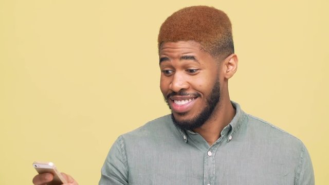 portrait of metis handsome guy with stylish haircut reading funny news good information on mobile phone laughing isolated over yellow background closeup. Concept of emotions