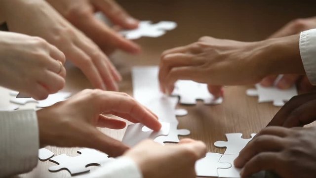 Close up view of hands assembling jigsaw puzzle on table, group of business people matching pieces playing board game, right decision making in business, help and support in teamwork concept