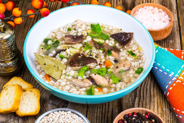 Vegetarian soup with mushrooms and pearl barley for lunch on wooden table