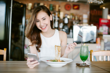 Young Asia woman eating food at restaurant and using on smart phone