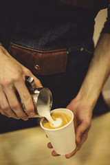 Unrecognizable bartender pouring cream for latte to takeaway paper cup.