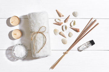 Spa set with sea salt, essential oil, soap and towel decorated with seashells on white wooden background