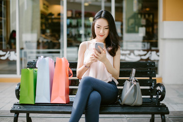 Young woman at the street with shopping bags and using mobile phone