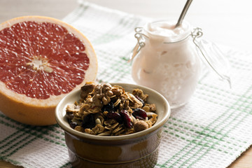 Granola from several types of cereals with nuts, coconut shavings and dried cranberries. Jar with homemade yogurt and grapefruit