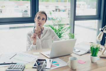 Development, authority, feminity concept. Pretty business woman is sitting at her light modern work spot in front of digital device, looking far, thoughtful, ponder, holding black trendy specs