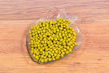 Canned green peas in a glass plate in the form of fish close-up on the table.