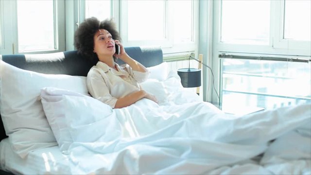 Young woman making phone call over mobile phone while lying on the bed