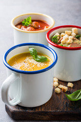 Assorted delicious homemade soups in enamel mugs with ingredients. Healthy food concept
