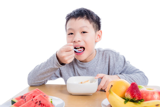 Young Asian Boy Eating Cereal With Yogurt For Breakfast Over White Background