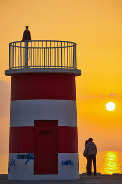 A couple in a lighthouse at sunset in Nazare, Portugal