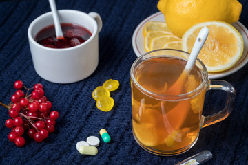 Still life of tea with lemon, tablets and thermometer, jam and berries. The concept of treating colds