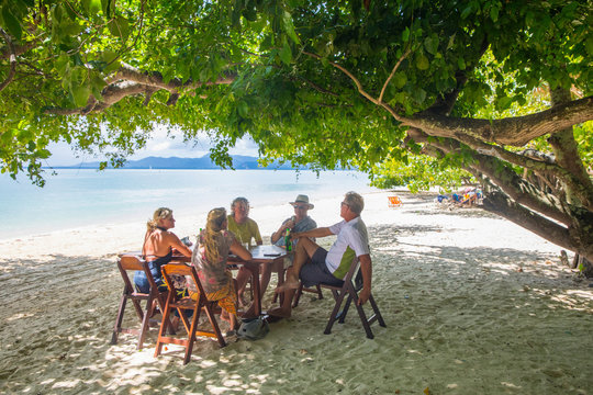 Friends relaxing at dining table on beach, Koh Rang Yai, Thailand, Asia