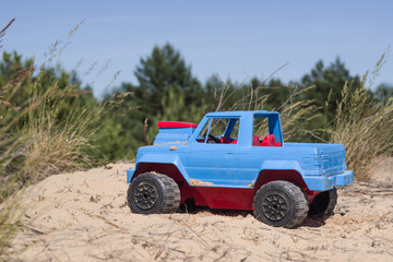 Fototapeta premium Toy red blue pickup in the sand of a green forest background.