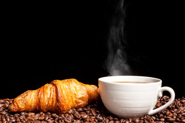 Croissant and steaming coffee beans in close up photo. Delicious morning drink and snack