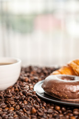 Coffee beans, donut and a cup of coffee in close up photo