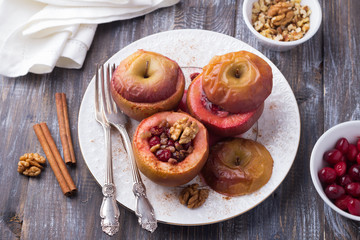 Obraz na płótnie Canvas Baked apples stuffed with cranberries, walnuts and honey with cinnamon on a white plate on a wooden table, selective focus. Delicious healthy vegan dessert