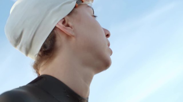 Low angle with close up of female swimmer wearing cap and goggles shaking her head and getting water out of ear, then gazing into distance