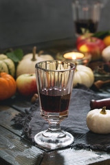 Autumn holiday table decoration setting with decorative pumpkins, apples, red leaves, glasses of red wine, candle over wooden table. Rustic style, day light