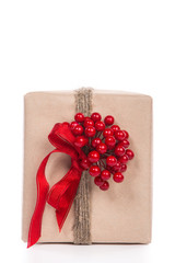 Christmas gift wrapped in craft and decorateed with twine with a boquette of little red berries isolated on white background