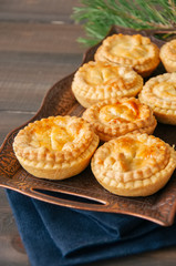 Mini meat pies from flaky dough on a vintage tray over wooden background.