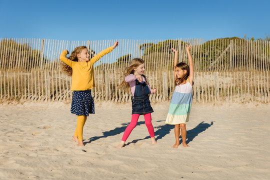 Three little girls dancing on a sandy beach