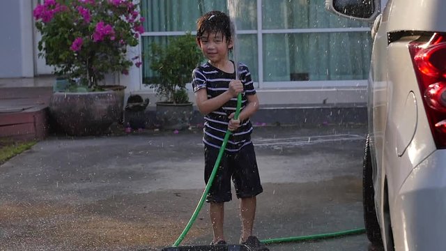 Cute asian boy has fun playing in water from a hose outdoors slow motion  