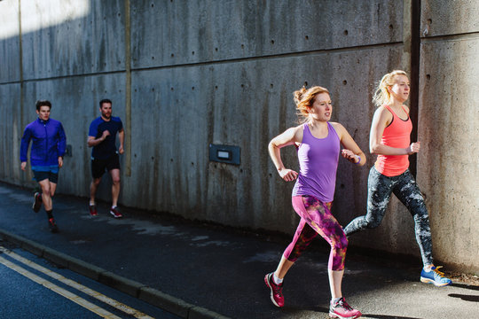 Four young adult runners running along city sidewalk