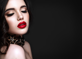 Beautiful woman portrait. Young lady posing close up on black background. Glamour make up, red lipstick. Gorgeous jewelry on neck.