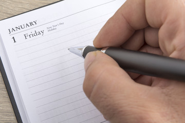 Man's hand holds a metal pen ready to set goals for the new year