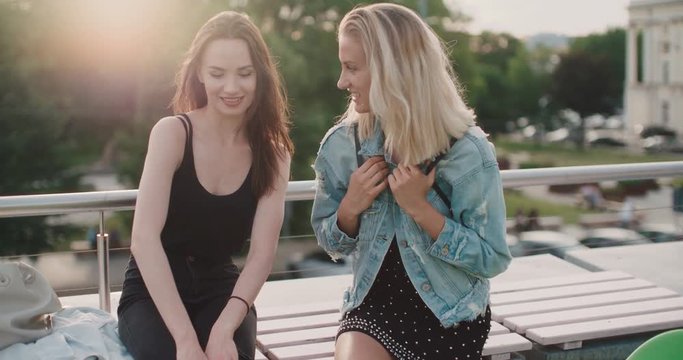 Beautiful young girls relaxing on a rooftop in a city. Portrait of two happy girls discussing latest gossip news. Positive face expressions, emotions, feelings, body language.