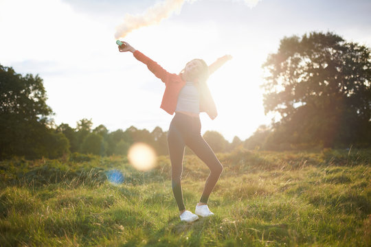 Young woman letting off smoke flare in sunlit field