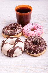 Different type of donuts on white wooden background next to a glass of cola. Delicious junk food