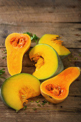 Cut ripe orange pumpkin with seeds and herbs on rustic wooden background. Vegetarian and raw organic healthy food concept, diet. Top view, copy space