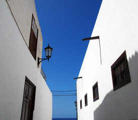 street of traditional white houses in perspective view looking upwards with bright blue summer sky leading to the sea