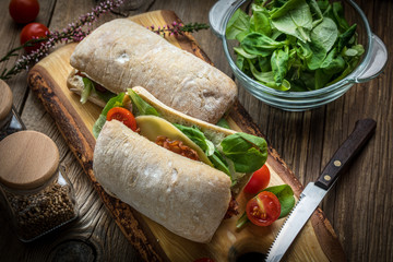 Ciabatta sandwich with arugula salad, bacon and yellow cheese.