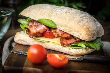 Ciabatta sandwich with arugula salad, bacon and yellow cheese.