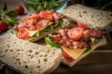 Ciabatta sandwich with arugula salad, bacon and yellow cheese.