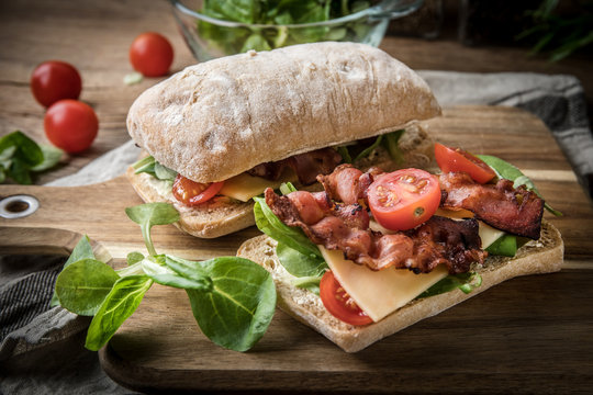 Ciabatta sandwich with arugula salad, bacon and yellow cheese.