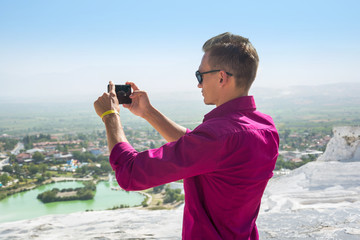 Young man in sunglasses, tourist, takes pictures with his mobile phone view Pamukkale, Turkey