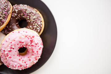 Over top view of delicious donuts on black plate on white surface