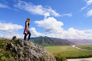 Woman stands on edge of cliff and looking at sun valley and mountains