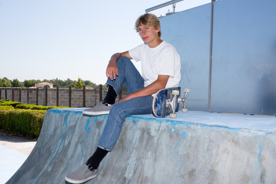 Sport conceptual image. Teenage skateboarder sits in skate-park